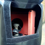 a flap in a black pvc gas bottle cover wit ha velcro flap to access the regulator fitting